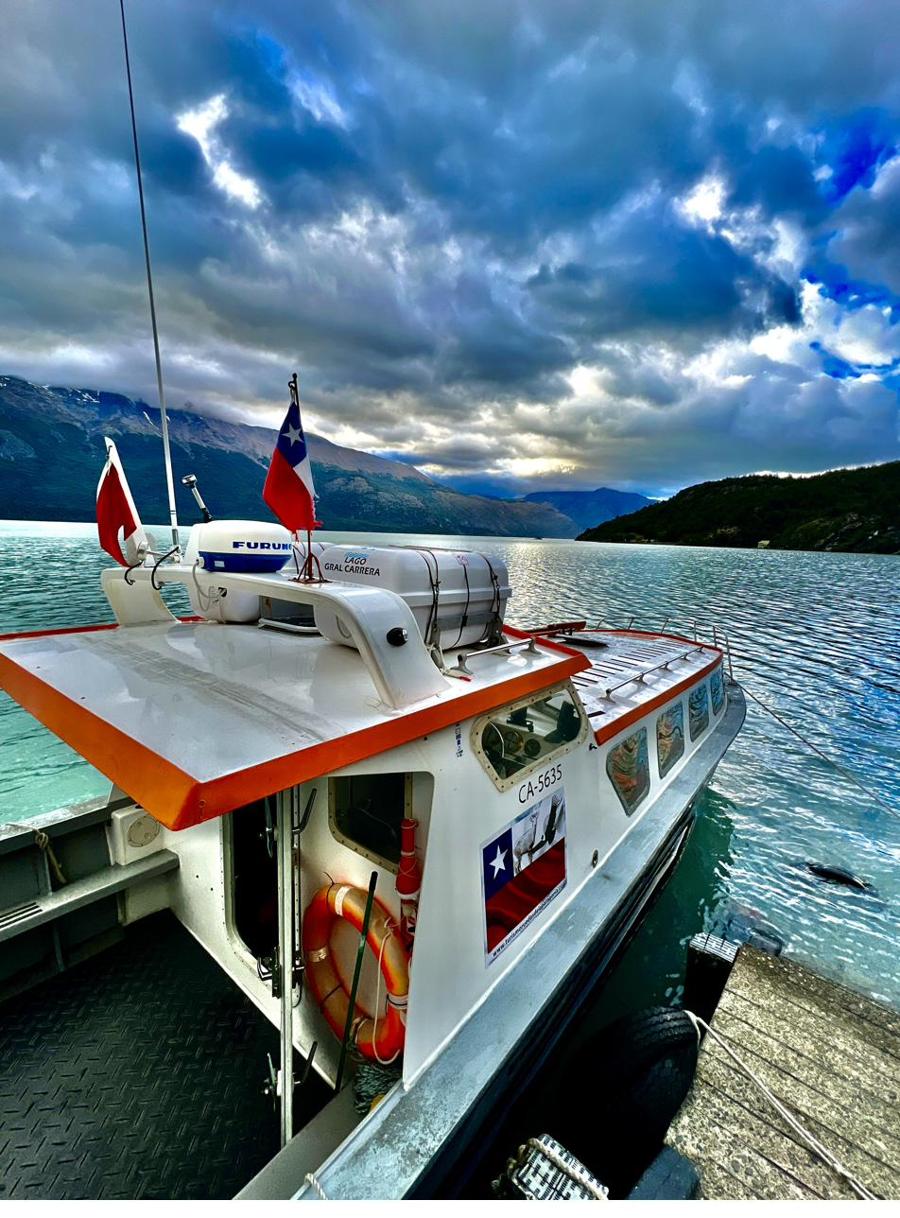 La embarcación de Ruedas de la Patagonia amarrada en el muelle, con la bandera chilena y el lago detrás